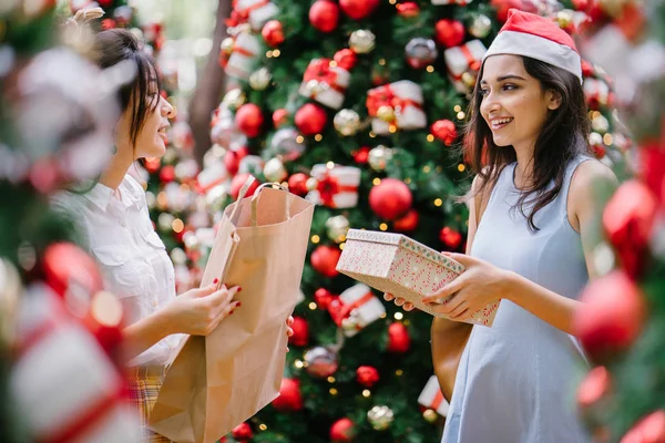 İki genç Asyalı kızlar exchange bir başka gün boyunca şehrin bir sokakta bir şekilde dekore edilmiş bir Noel ağacı altında sunuyor. Hint, diğer Çinli biri