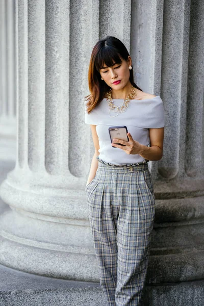 Çekici, kendine güvenen ve başarılı bir Çinli Asyalı kadının portresi. Akıllı telefonunu tutuyor. 