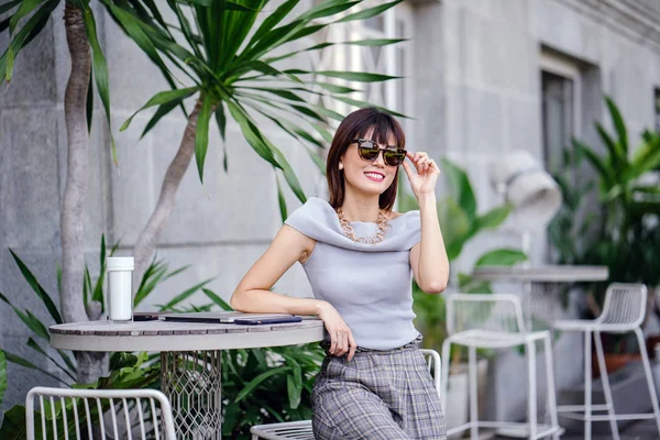 Açık havada şık bir yerde oturan bir emin, şık ve çekici orta yaşlı Çinli Asyalı kadın portresi. O bir pohpohlama gri kıyafeti giyiyor.