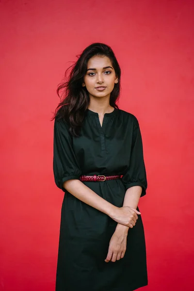 スタジオの赤いスタジオを背景に美しい 魅力的なインド アジアの女性の肖像画 彼女はシンプルな緑のドレスと赤帯のエレガントな服を着て 笑顔です — ストック写真