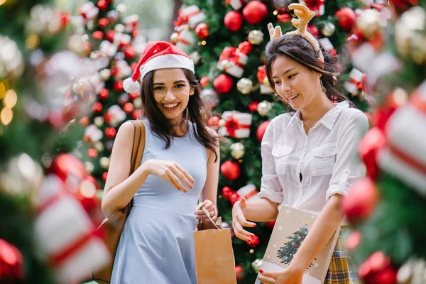 İki genç Asyalı kızlar exchange bir başka gün boyunca şehrin bir sokakta bir şekilde dekore edilmiş bir Noel ağacı altında sunuyor. Hint, diğer Çinli biri