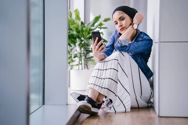 日中はオフィスやコワーキングスペース 図書館の一角に若い中東のムスリム女性がいて スマートフォンを使っています スカーフ ヒジャーブ をかぶっている — ストック写真