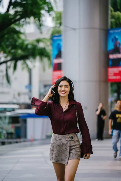 beautiful Korean woman in an elegant blouse and shorts dancing as she walks down a street in the city with her headphones on