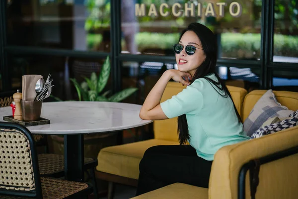 Genç ve çekici Çinli Asyalı bir kadının portresi uzanarak ve bir hafta sonu gün boyunca bir kafede rahatlatıcı. Nane yeşili bir kazak giyiyor.