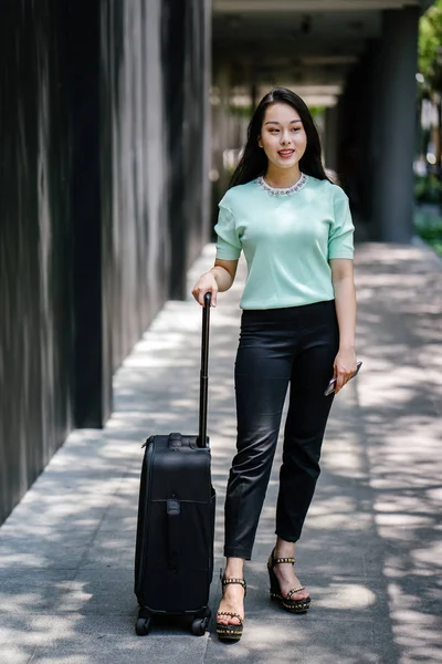 Genç bir Asyalı kadın bavulunu çekiyor. O çekici, zarif ve şık giyinmiş