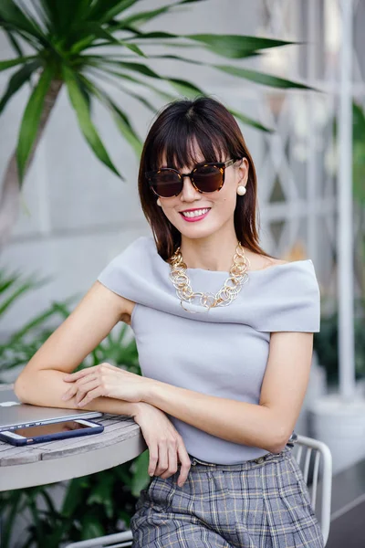 Açık havada şık bir yerde oturan bir emin, şık ve çekici orta yaşlı Çinli Asyalı kadın portresi. O bir pohpohlama gri kıyafeti giyiyor.