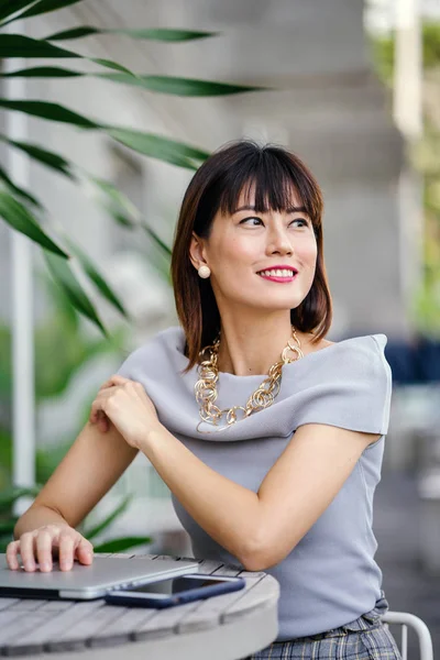 Açık havada şık bir yerde oturan bir emin, şık ve çekici orta yaşlı Çinli Asyalı kadın portresi. O bir pohpohlama gri kıyafeti giyiyor.