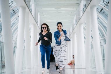 İki farklı arkadaş, iyi aydınlatılmış beyaz fütüristik bir üstgeçit köprüsünden kameraya doğru koşuyorlar. Biri Müslüman bir Orta Doğulu kadın, diğeri de Çinli..