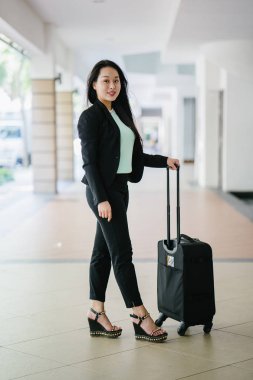 Genç bir Asyalı kadın bavulunu çekiyor. O çekici, zarif ve şık giyinmiş