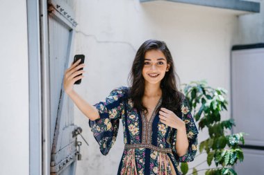 O kendini bir selfie onun smartphone ile alır gibi gülümseyen güzel bir elbise içinde bir genç Hintli Asyalı kadın portresi