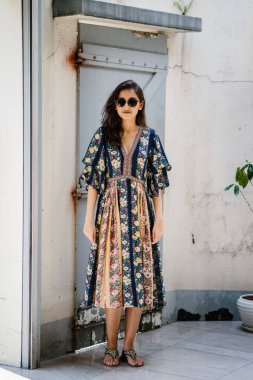 uzun boylu, zarif ve güzel Hint Asyalı kadın yaz elbise ve güneş gözlüğü gülümsüyor o pozlar gün boyunca bir arka sokakta bir sokakta olarak içinde