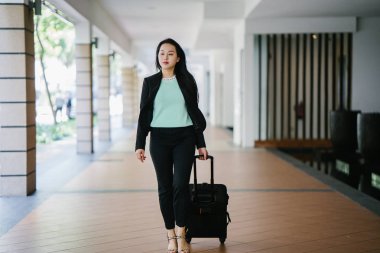 Genç bir Asyalı kadın bavulunu çekiyor. O çekici, zarif ve şık giyinmiş