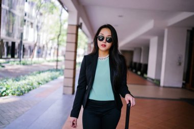 Genç bir Asyalı kadın bavulunu çekiyor. O çekici, zarif ve şık giyinmiş