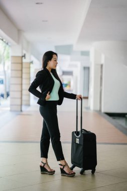 Genç bir Asyalı kadın bavulunu çekiyor. O çekici, zarif ve şık giyinmiş