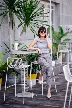 Açık havada şık bir yerde oturan bir emin, şık ve çekici orta yaşlı Çinli Asyalı kadın portresi. O bir pohpohlama gri kıyafeti giyiyor.