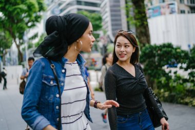İki arkadaş, Orchard Road, Singapur, Asya 'da aydınlık bir yaz gününde mutlu bir şekilde yürüyüp konuşurlar. Biri Müslüman Malezyalı, diğeri Çinli bir kadın.. 