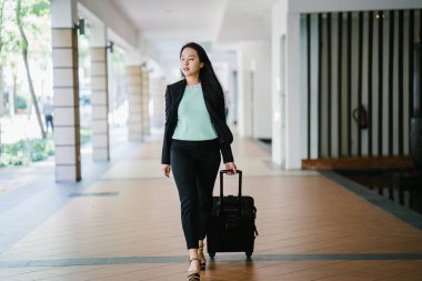 Genç bir Asyalı kadın bavulunu çekiyor. O çekici, zarif ve şık giyinmiş