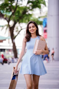 genç, son moda ve mutlu genç Hintli Asyalı kadın alışveriş bölgesine bir sokakta yürürken bir mavi elbiseli 