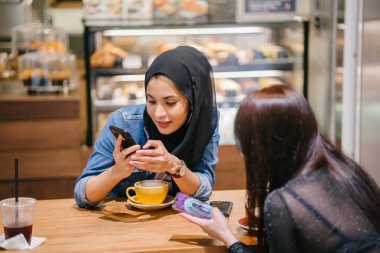 Çinli bir Asyalı kadın ve Müslüman bir kadın kafede eğleniyorlar.