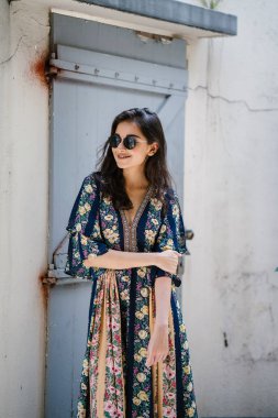 uzun boylu, zarif ve güzel Hint Asyalı kadın yaz elbise ve güneş gözlüğü gülümsüyor o pozlar gün boyunca bir arka sokakta bir sokakta olarak içinde