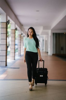 Genç bir Asyalı kadın bavulunu çekiyor. O çekici, zarif ve şık giyinmiş