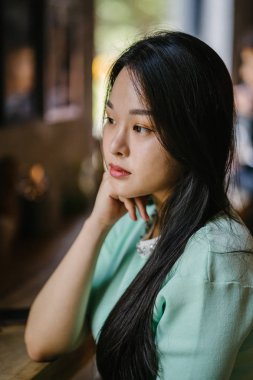 Genç ve çekici Çinli Asyalı bir kadının portresi uzanarak ve bir hafta sonu gün boyunca bir kafede rahatlatıcı. Nane yeşili bir kazak giyiyor.