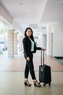 Genç bir Asyalı kadın bavulunu çekiyor. O çekici, zarif ve şık giyinmiş