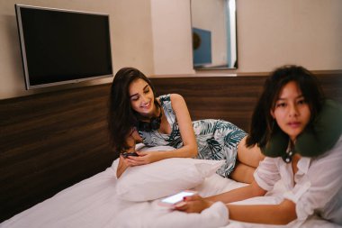 İki genç Asyalı arkadaş bir pansiyonda bir yatakta oturuyor. İkisi de Asyalı ve birlikte seyahat ediyorlar. Biri Hintli, diğeri Çinli. İkisi de gündelik giysiler içinde ve odalarında dinleniyorlar..