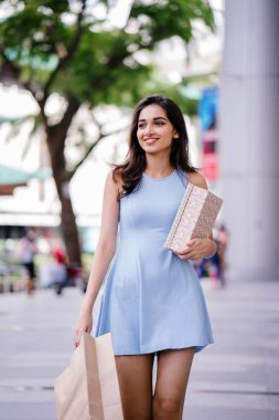 genç, son moda ve mutlu genç Hintli Asyalı kadın alışveriş bölgesine bir sokakta yürürken bir mavi elbiseli 