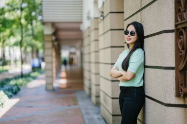 Gün boyunca bir taş duvara yaslanmış genç, seksi ve göz alıcı Asyalı bir kadının portresi. Siyah pantolonuna uyacak nane yeşili bir kazak giyiyor.