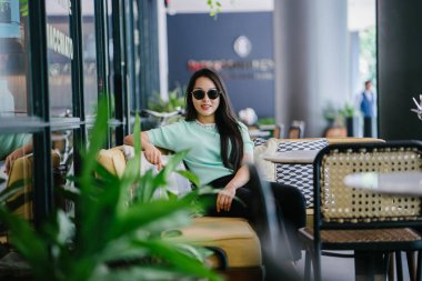 Genç ve çekici Çinli Asyalı bir kadının portresi uzanarak ve bir hafta sonu gün boyunca bir kafede rahatlatıcı. Nane yeşili bir kazak giyiyor.