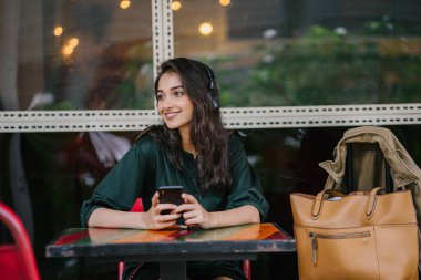 Genç Hintli Asyalı kadın o onun Smartphone-e doğru onun kulaklık streaming müzik hoşlanır