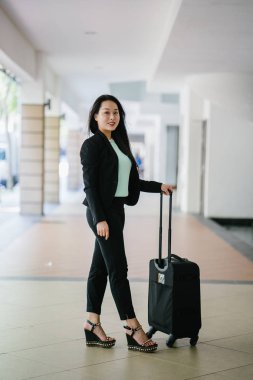 Genç bir Asyalı kadın bavulunu çekiyor. O çekici, zarif ve şık giyinmiş