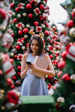 Genç, güzel ve mutlu bir Hint Asyalı kadın şenlikli Noel portresi bir hediye bir Noel ağacı önünde tutan gülümseyerek.