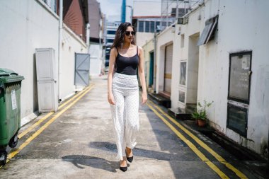 Genç, uzun boylu, ince ve zarif Hint Asyalı kadın rahat bir kıyafet içinde Asya bir sokakta bir sokakta aşağı gün boyunca yürür