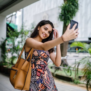Genç, güzel ve zarif Punjabi Hint Asyalı kadın kendini bir selfie onun smartphone ile yoğun bir cadde üzerinde gün boyunca alır