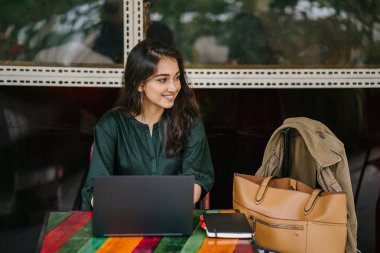 genç üniversite öğrencisi (Hint Asyalı kadın) eğitim ve gün boyunca dizüstü bilgisayar bir masa başında çalışma