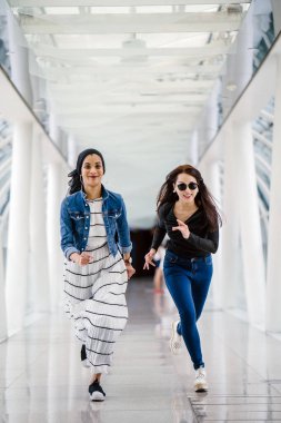 İki farklı arkadaş, iyi aydınlatılmış beyaz fütüristik bir üstgeçit köprüsünden kameraya doğru koşuyorlar. Biri Müslüman bir Orta Doğulu kadın, diğeri de Çinli..