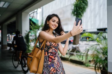 Genç, güzel ve zarif Punjabi Hint Asyalı kadın kendini bir selfie onun smartphone ile yoğun bir cadde üzerinde gün boyunca alır