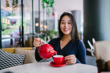 Bir açık havada açık havada oturan ve kırmızı bir çay seti çay sıcak bir fincan zevk genç, çekici, zarif ve güzel Asyalı kadın Portresi. 