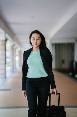 Genç bir Asyalı kadın bavulunu çekiyor. O çekici, zarif ve şık giyinmiş