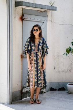 uzun boylu, zarif ve güzel Hint Asyalı kadın yaz elbise ve güneş gözlüğü gülümsüyor o pozlar gün boyunca bir arka sokakta bir sokakta olarak içinde