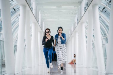 İki farklı arkadaş, iyi aydınlatılmış beyaz fütüristik bir üstgeçit köprüsünden kameraya doğru koşuyorlar. Biri Müslüman bir Orta Doğulu kadın, diğeri de Çinli..