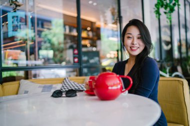 Bir açık havada açık havada oturan ve kırmızı bir çay seti çay sıcak bir fincan zevk genç, çekici, zarif ve güzel Asyalı kadın Portresi. 