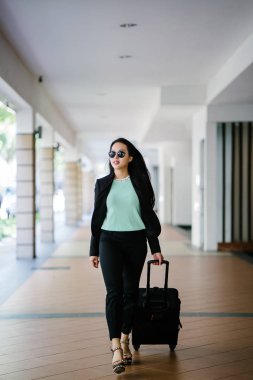 Genç bir Asyalı kadın bavulunu çekiyor. O çekici, zarif ve şık giyinmiş