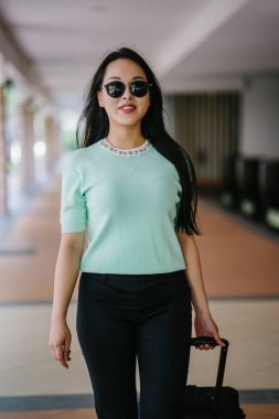 Genç bir Asyalı kadın bavulunu çekiyor. O çekici, zarif ve şık giyinmiş