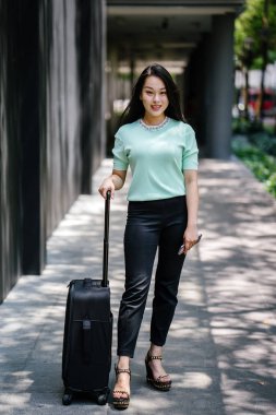 Genç bir Asyalı kadın bavulunu çekiyor. O çekici, zarif ve şık giyinmiş
