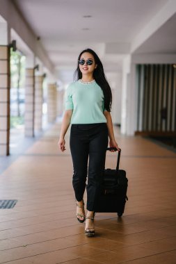Genç bir Asyalı kadın bavulunu çekiyor. O çekici, zarif ve şık giyinmiş