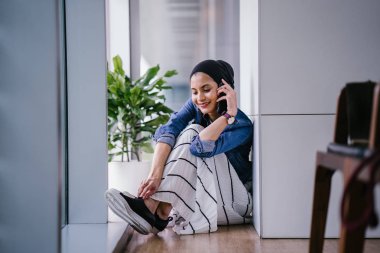 Genç bir Ortadoğulu Müslüman kadın gün boyunca bir ofiste, ortak çalışma alanında veya kütüphanede oturuyor ve akıllı telefonunu kullanıyor. Başörtüsü takıyor (başörtüsü)).