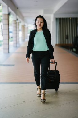 Genç bir Asyalı kadın bavulunu çekiyor. O çekici, zarif ve şık giyinmiş